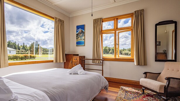 Habitación de hotel con dos camas, un aparador de madera, una silla, un ventanal grande con cortinas, un cuadro y un espejo.