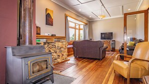 Una sala de estar con estufa de leña, chimenea de piedra, sofá, televisor y un ventanal.