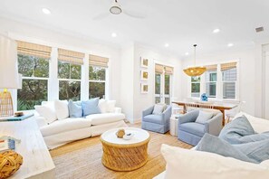 A spacious living room with a white sofa, a blue armchair, a round coffee table, and a dining area with a white table and chairs.