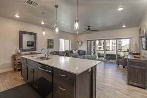 A spacious kitchen with a central island, a dining area with a sofa, and a balcony with outdoor seating. - Estancia Pool Resort S 301 | Poolside View (Saint George)
