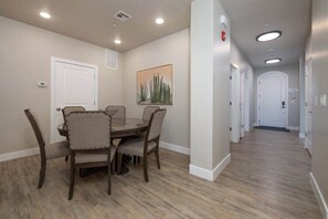 A dining area with a round table and chairs, a painting on the wall, and a hallway with doors. - Estancia Pool Resort S 301 | Poolside View (Saint George)
