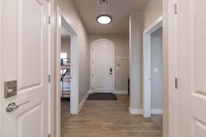 A hallway with a wooden floor, white walls, and a white door at the end. - Estancia Pool Resort S 301 | Poolside View (Saint George)