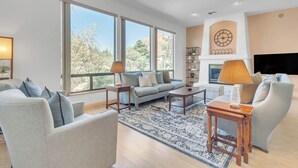A spacious living room with a large sofa, two armchairs, a coffee table, and a TV. There are large windows providing a view of the outdoors. - Discover Sedona Peaceful Oasis: a serene 3BR retreat with stunning Red Rock views. (Sedona)