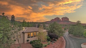 A modern house with a large window, surrounded by a well-maintained garden, set against a backdrop of red rock formations and a sunset sky. - Discover Sedona Peaceful Oasis: a serene 3BR retreat with stunning Red Rock views. (Sedona)