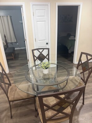 Un coin repas avec une table en verre entourée de chaises, une porte blanche et une pièce visible au fond.