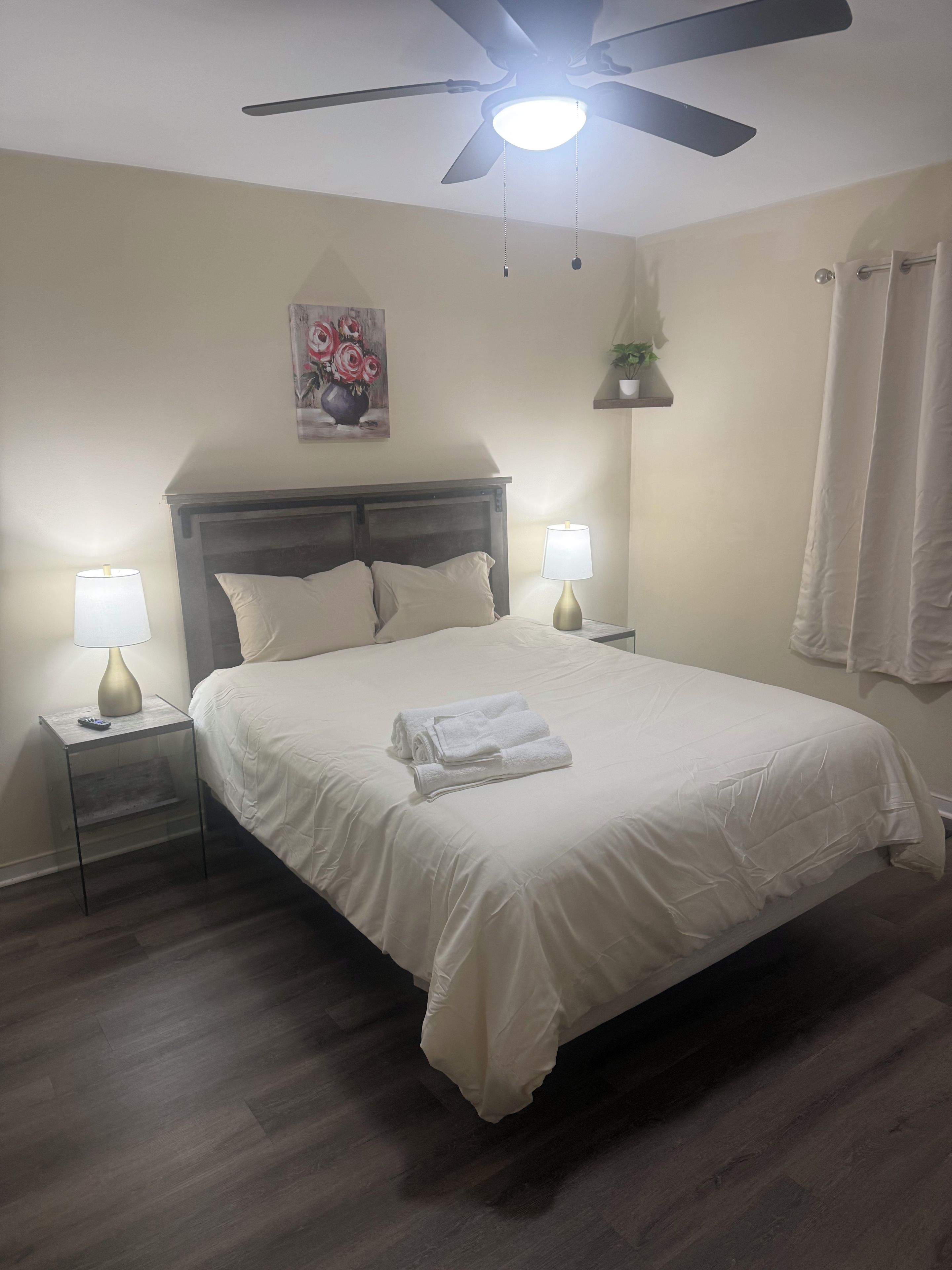 Une chambre à coucher avec un lit, deux lampes de chevet, un ventilateur de plafond et une étagère fixée au mur, sur laquelle est posée une plante.