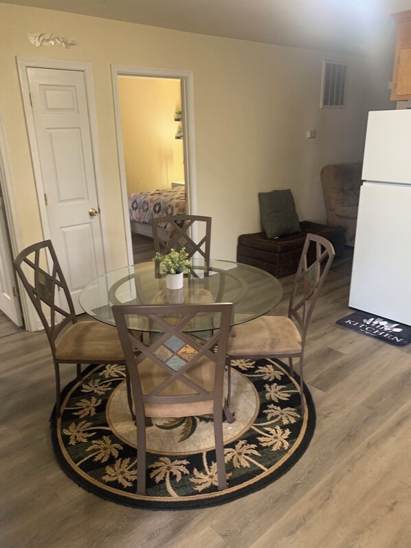Un coin repas avec une table en verre entourée de quatre chaises, un petit vase avec des fleurs et un tapis à motifs.