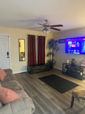A living room with a sofa, a coffee table, a television, a ceiling fan, and a potted plant. - Cozy three bedroom fully furnish house
 (Ettrick)