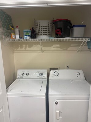 A laundry room with two front-loading washing machines, a shelf with laundry supplies, and a basket. - Cozy three bedroom fully furnish house
(Ettrick)