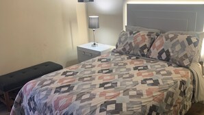 Ein Schlafzimmer mit einem Bett, einem Nachttisch mit Lampe, einer Bank und einem an der Wand befestigten Regal mit Pflanze.