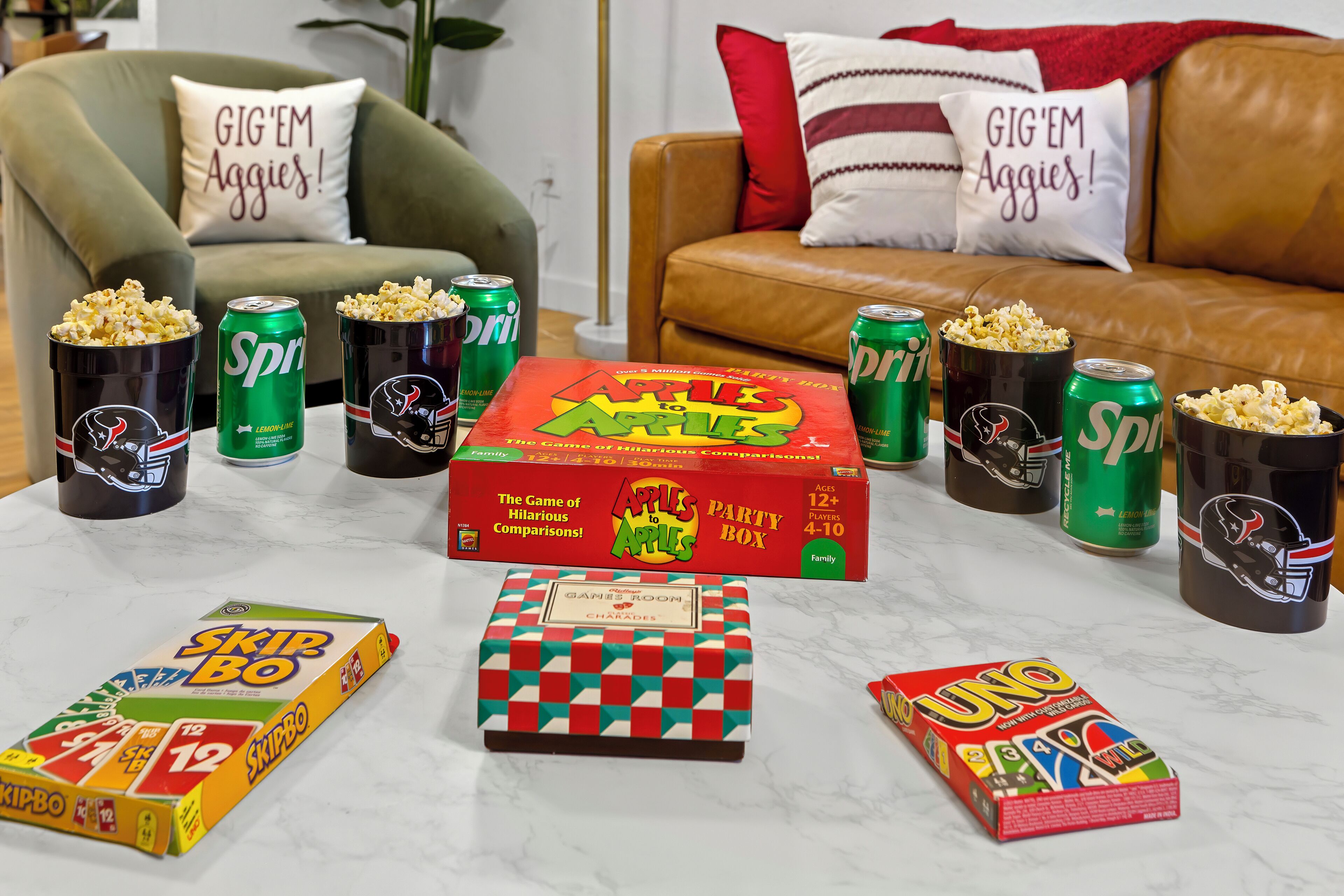 A living room with a couch, pillows, and a table with party games and snacks.