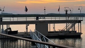 En brygga med utsikt över solnedgången över vattnet, med en liten båt, en livboj och en flagga.