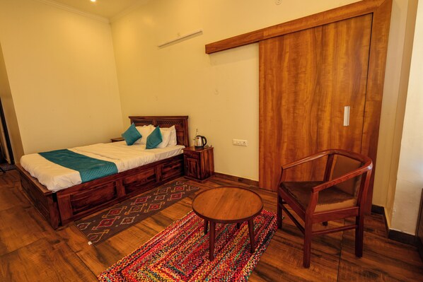 Un dormitorio con una cama de madera, una mesita redonda pequeña, una silla y una alfombra colorida.