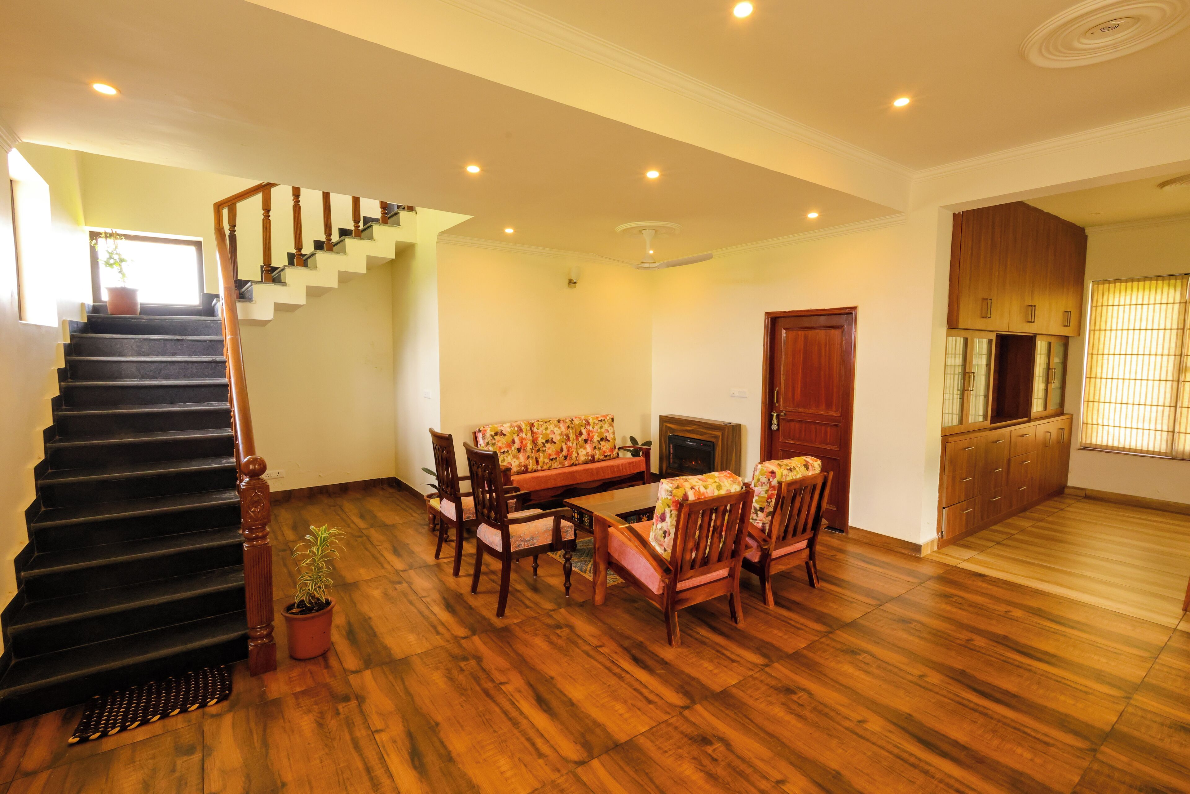 A spacious living area with a wooden staircase, a sofa set, and a dining table.