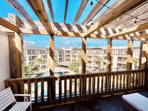 A wooden balcony with a view of a pool and a multi-story building.