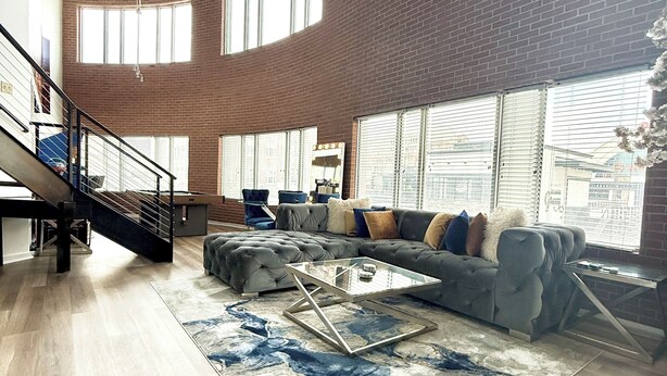 A spacious living area with a large sectional sofa, a glass coffee table, and a patterned rug. There is a staircase with a metal railing leading to an upper level. -  Stylish loft, centered in the heart of Atlantic station. (Atlanta)
