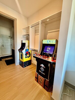 Una habitación con dos máquinas recreativas, una zona de ducha con azulejos y suelo de madera.