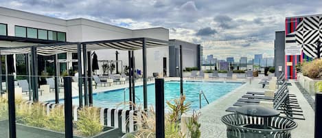 A rooftop pool area with lounge chairs, a pool, and potted plants.