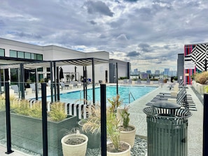 A rooftop pool area with lounge chairs, a pool, and potted plants.