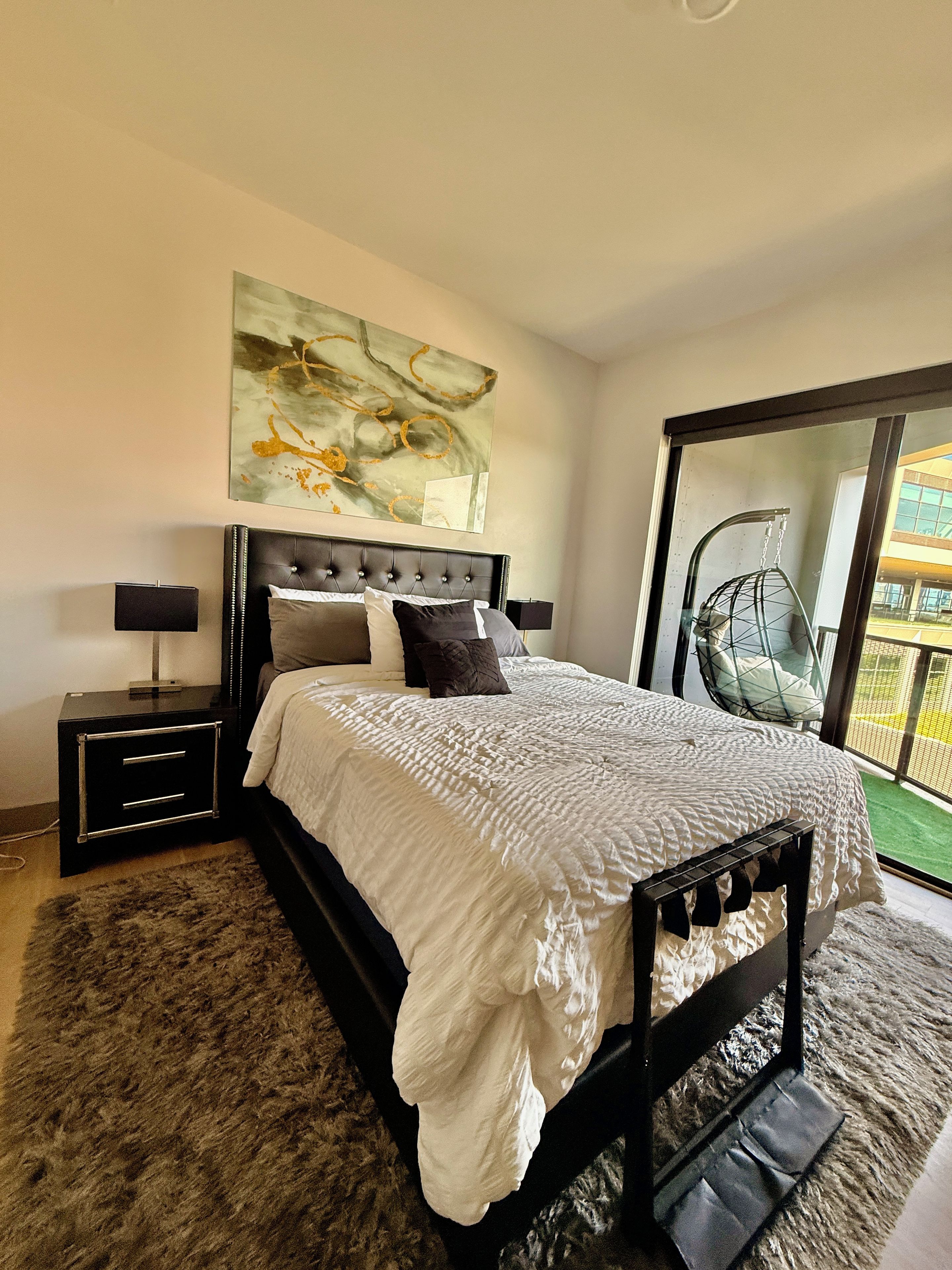 Una camera da letto con un letto, comodini, un quadro appeso e vista attraverso una porta vetrata.