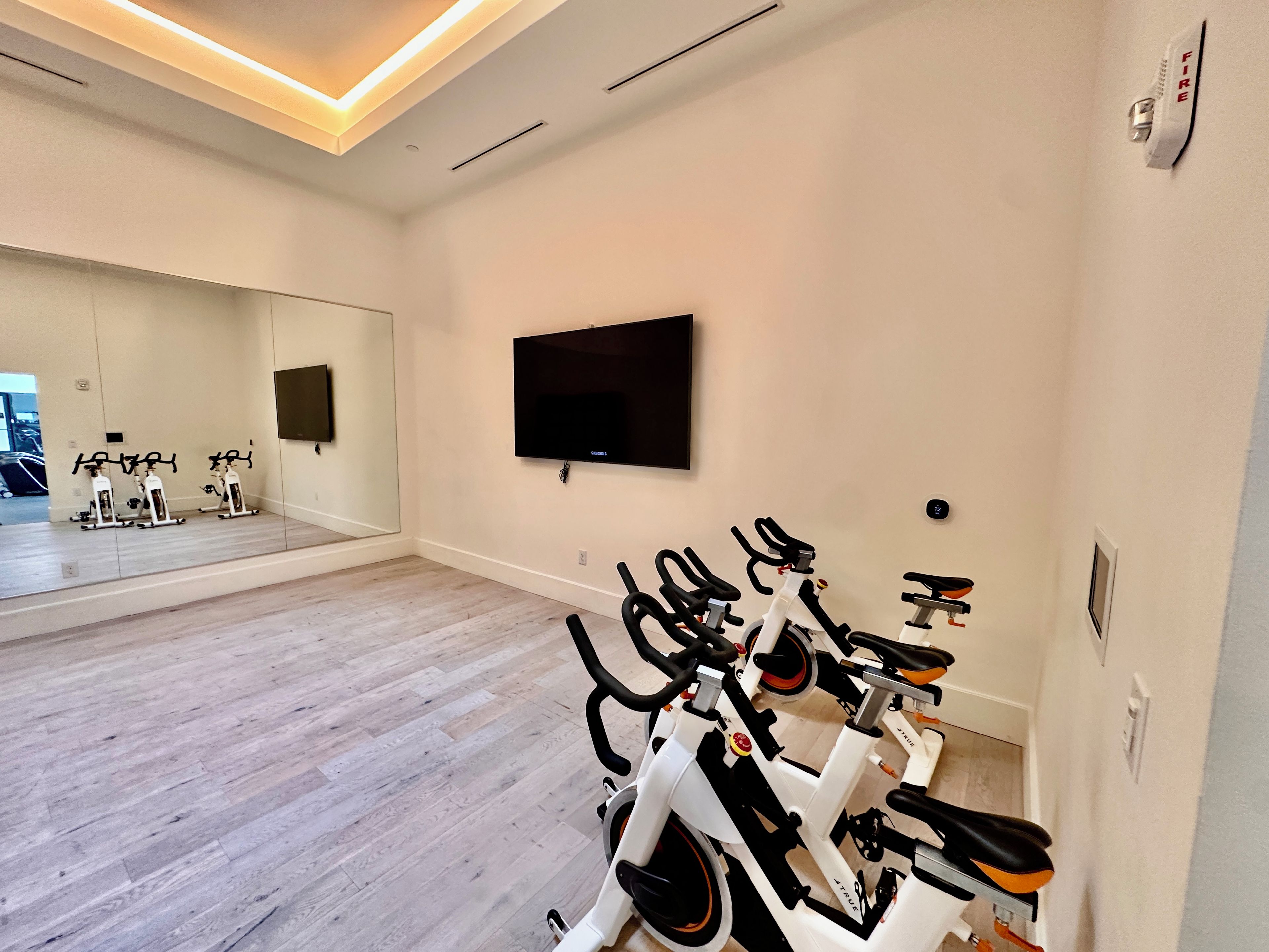 A gym with stationary bikes, a TV, and a large mirror.