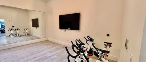 A gym with stationary bikes, a TV, and a large mirror.