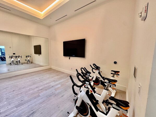 A gym with stationary bikes, a TV, and a large mirror.