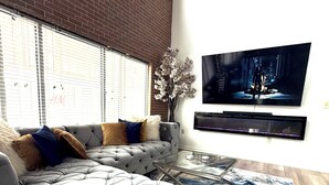 A modern living room with a large sectional sofa, a flat-screen TV mounted on the wall, and a decorative vase with flowers. -  Stylish loft, centered in the heart of Atlantic station. (Atlanta)