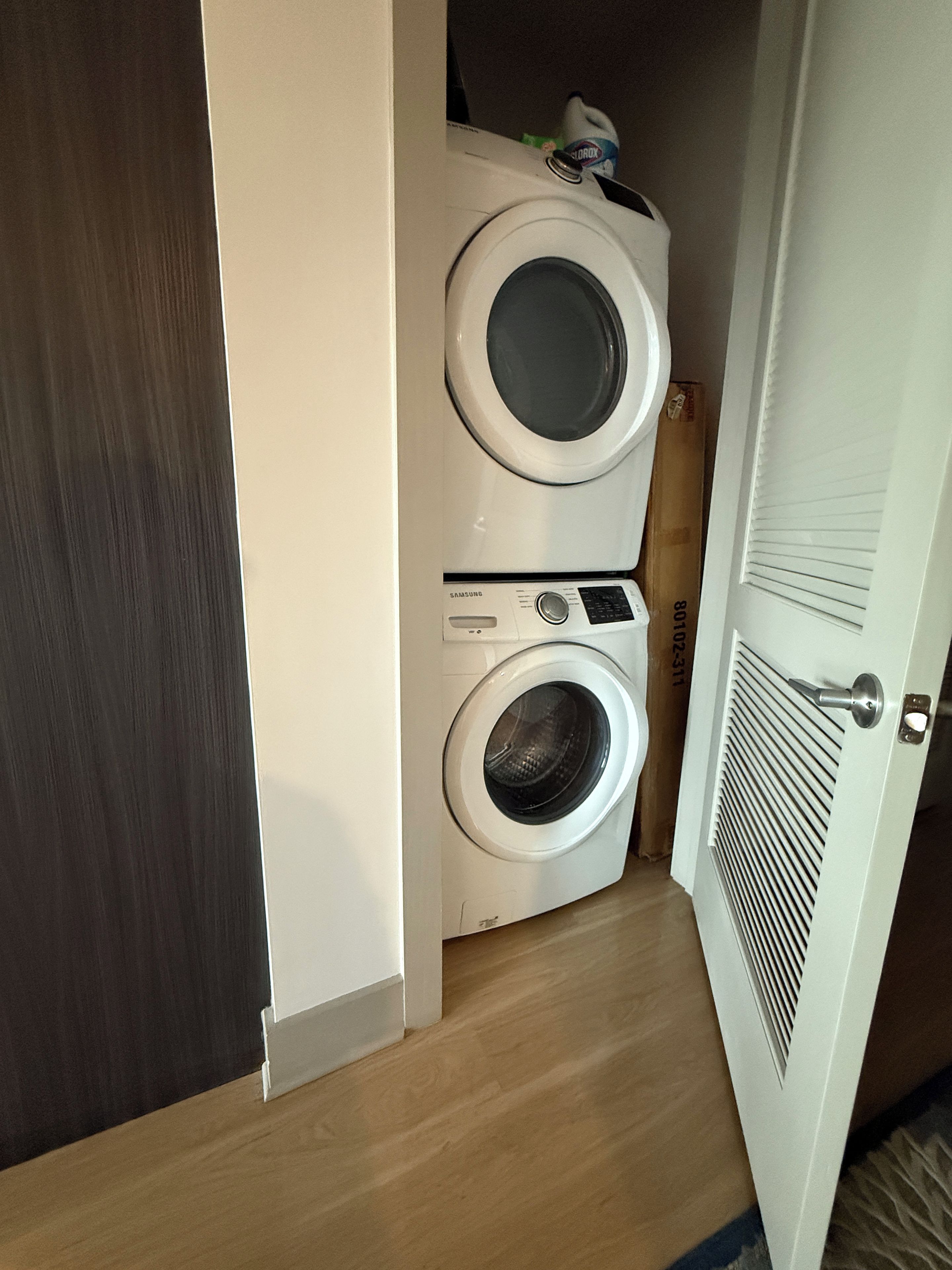 A laundry room with two stacked washing machines, a wooden floor, and a white door.