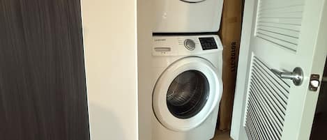 A laundry room with two stacked washing machines, a wooden floor, and a white door.