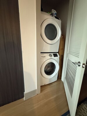 Un cuarto de lavado con dos lavadoras apiladas, piso de madera y una puerta blanca.