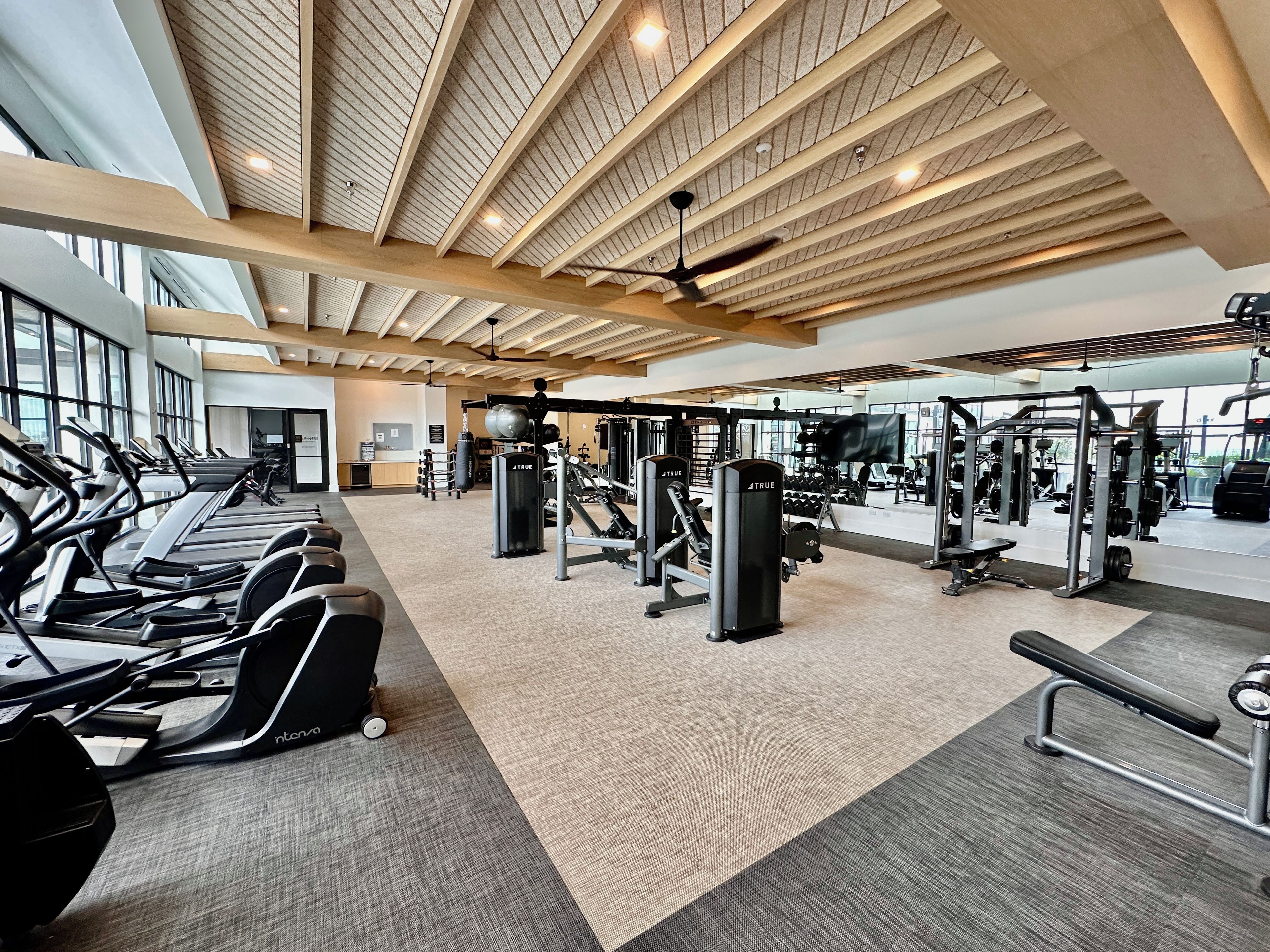 Un gimnasio con cintas de correr, máquinas de pesas y un techo de vigas de madera.