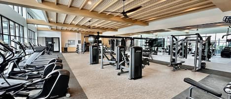 Une salle de sport équipée de tapis de course, d’appareils de musculation et dont le plafond est orné de poutres en bois.