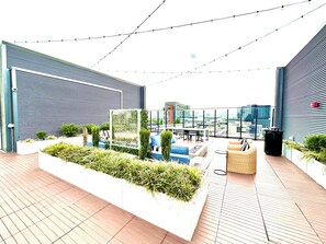 A rooftop terrace with a seating area, a planter with greenery, and a view of the cityscape.