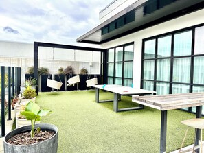 Un espacio exterior moderno con césped artificial, una mesa, sillas y plantas en macetas.