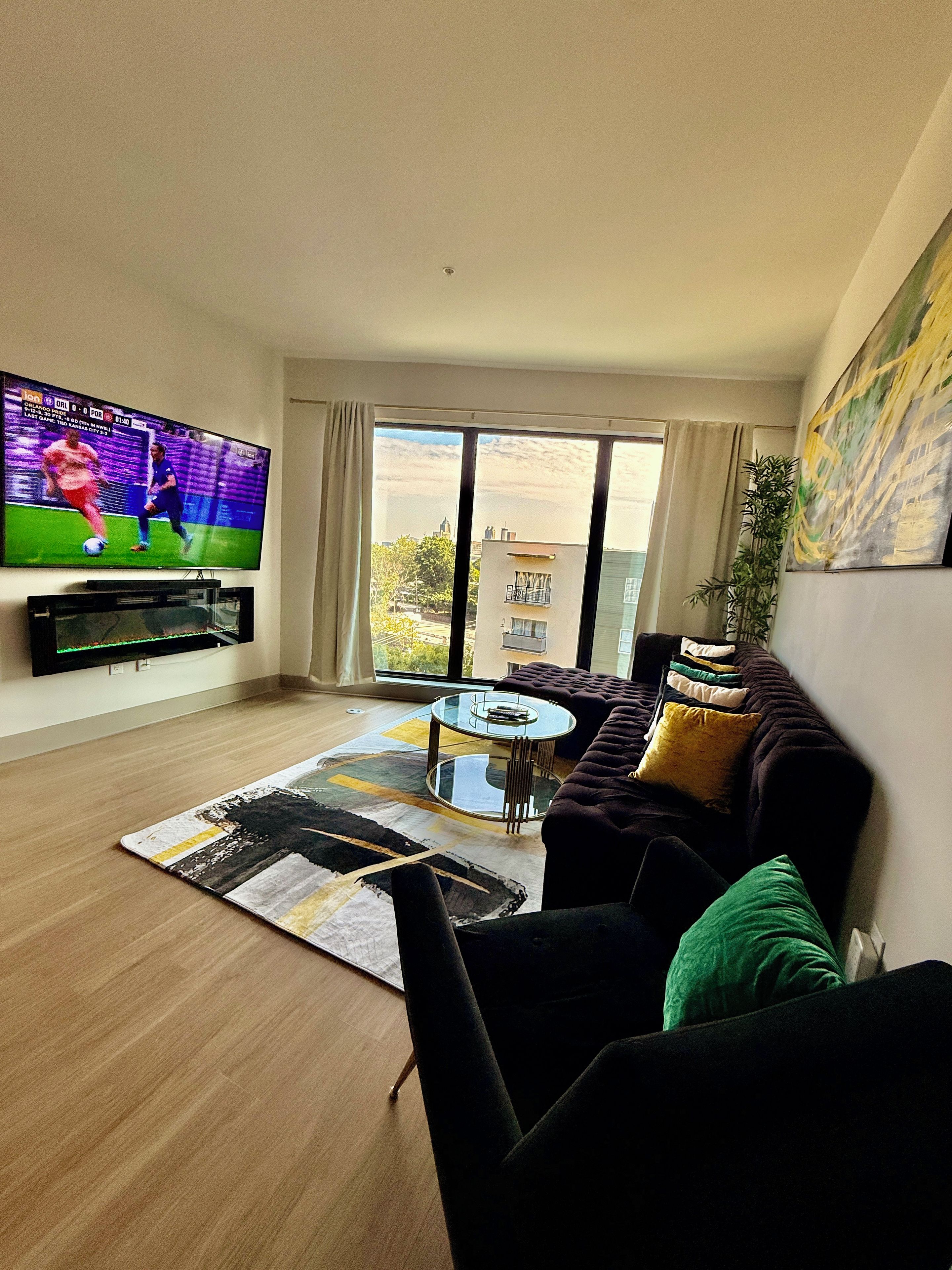Una sala de estar con un televisor de pantalla plana, un sofá, una mesa de centro y vistas amplias a través de grandes ventanales.