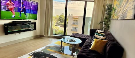 Una sala de estar con un televisor de pantalla plana, un sofá, una mesa de centro y vistas amplias a través de grandes ventanales.