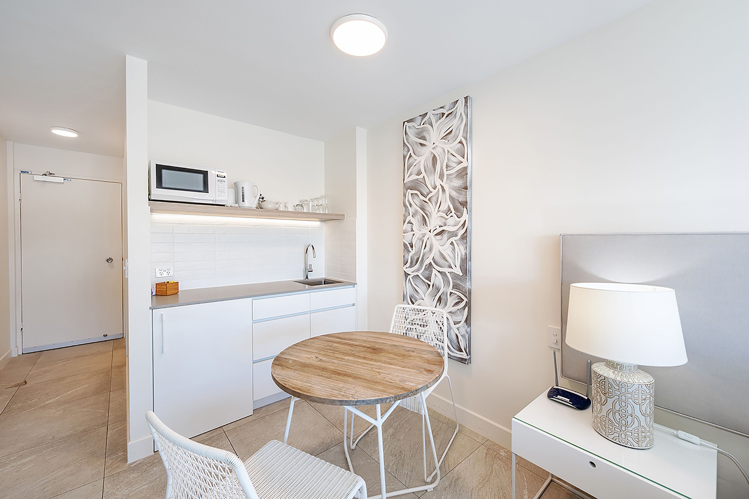 Una cocina moderna con armarios blancos, un microondas y una mesa de comedor de madera con sillas blancas.