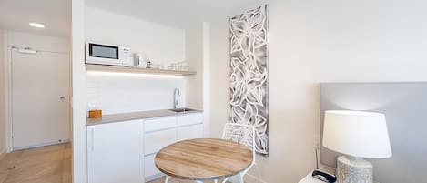Una cocina moderna con armarios blancos, un microondas y una mesa de comedor de madera con sillas blancas.