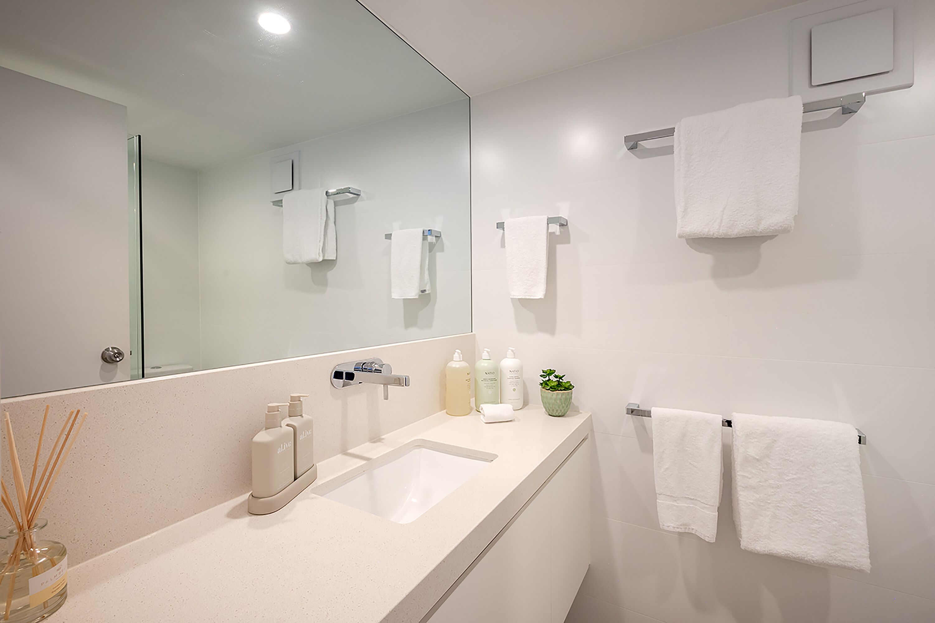 A modern bathroom with a large mirror, a white sink, and two towels hanging on a rack.