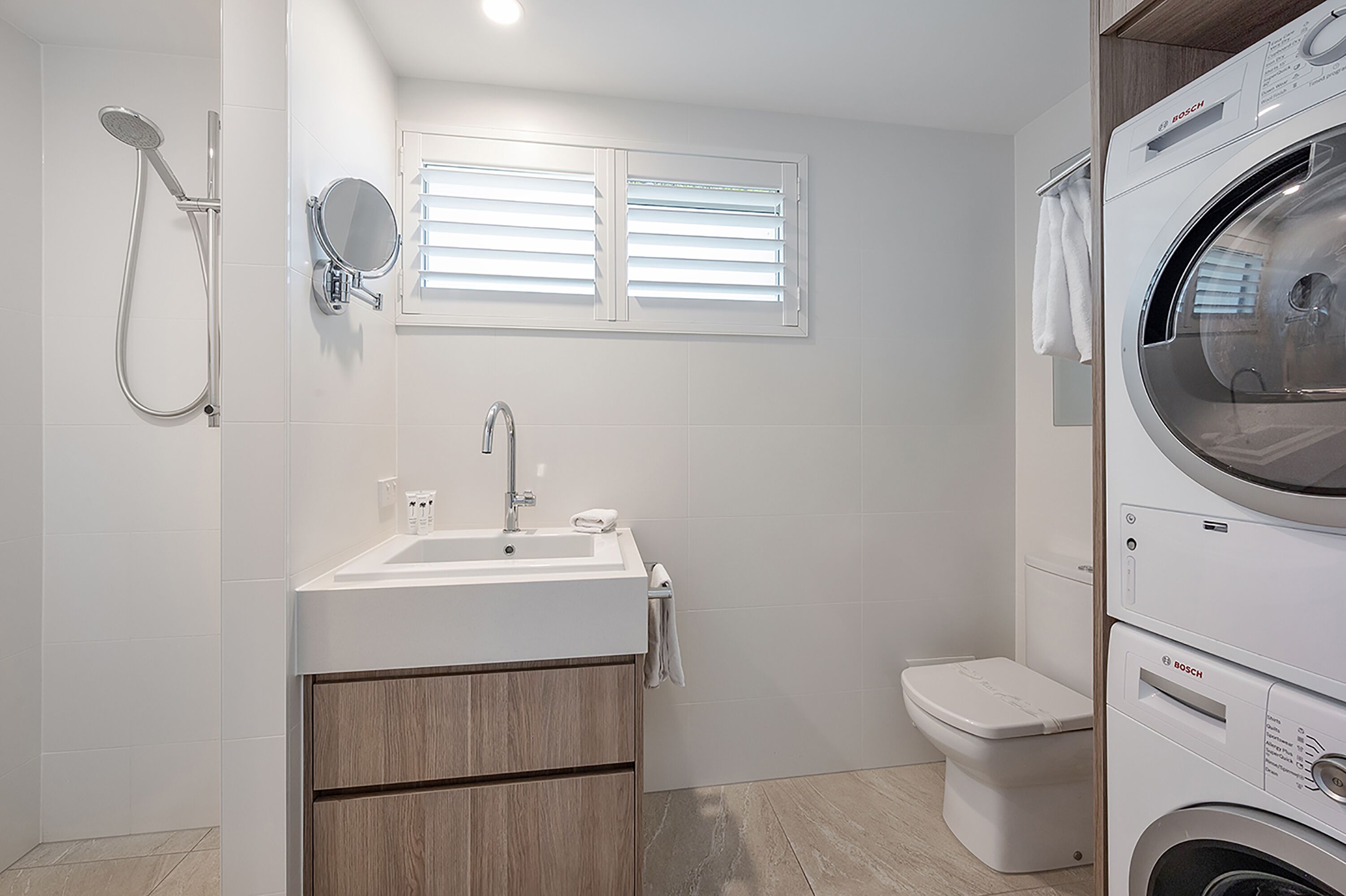 Un bany modern amb un lavabo, mirall, dutxa, vàter i una màquina de rentar Bosch.