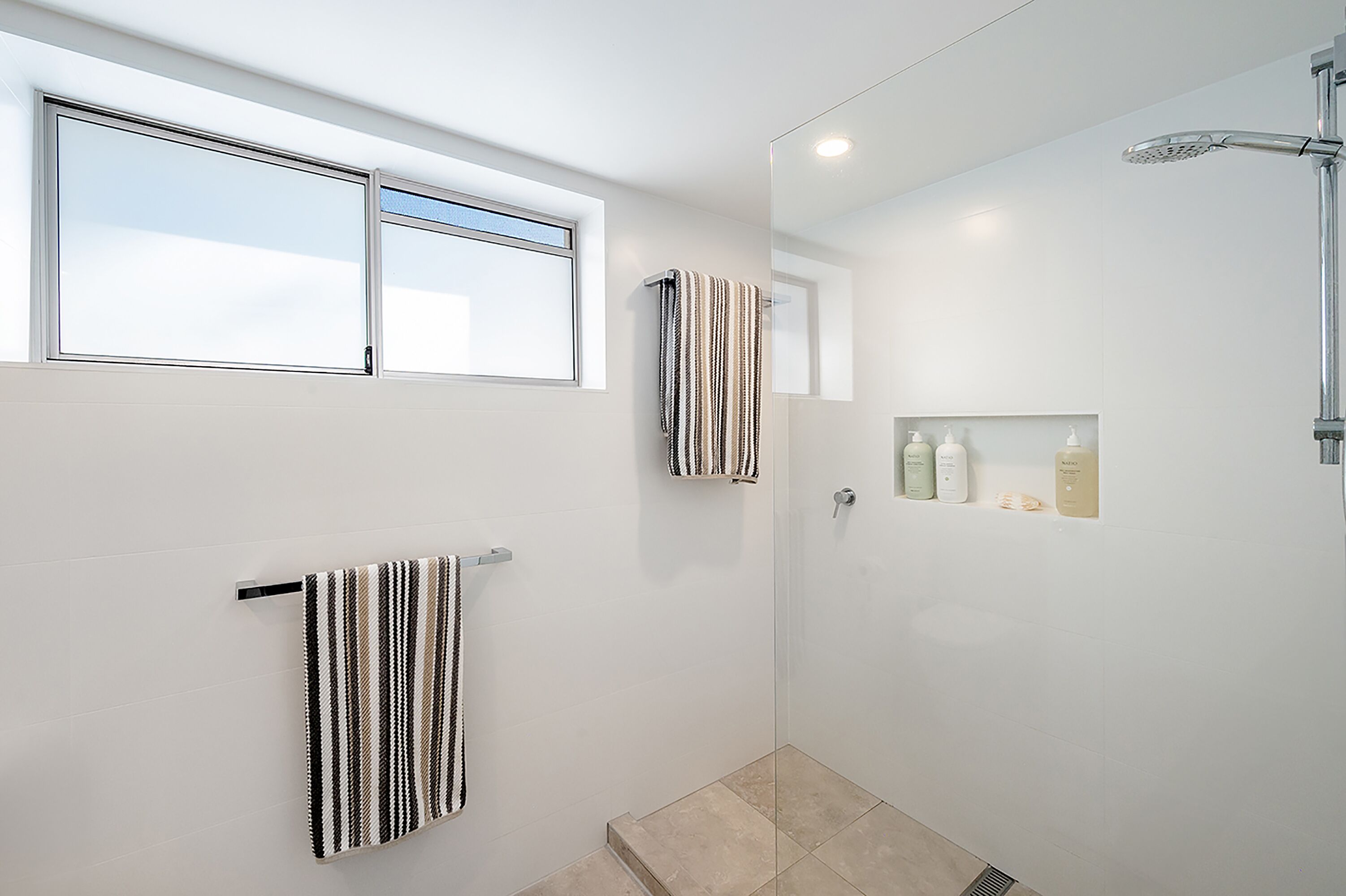 A modern bathroom with a shower, a window, and two towels hanging on the wall.