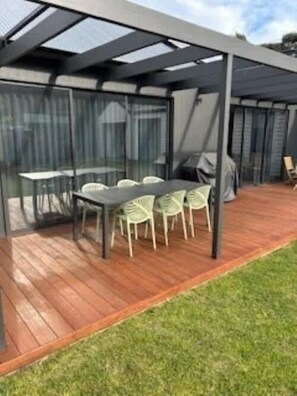 A covered outdoor seating area with a table and chairs, a grill, and a view of the surrounding landscape. - Tranquil Retreat (Blairgowrie)