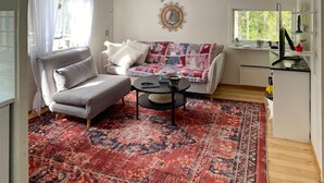 A living room with a grey sofa, a patterned rug, a coffee table, and a window with a view of trees. - 3 bedroom awesome home in Ljusterö (Ljusterö)