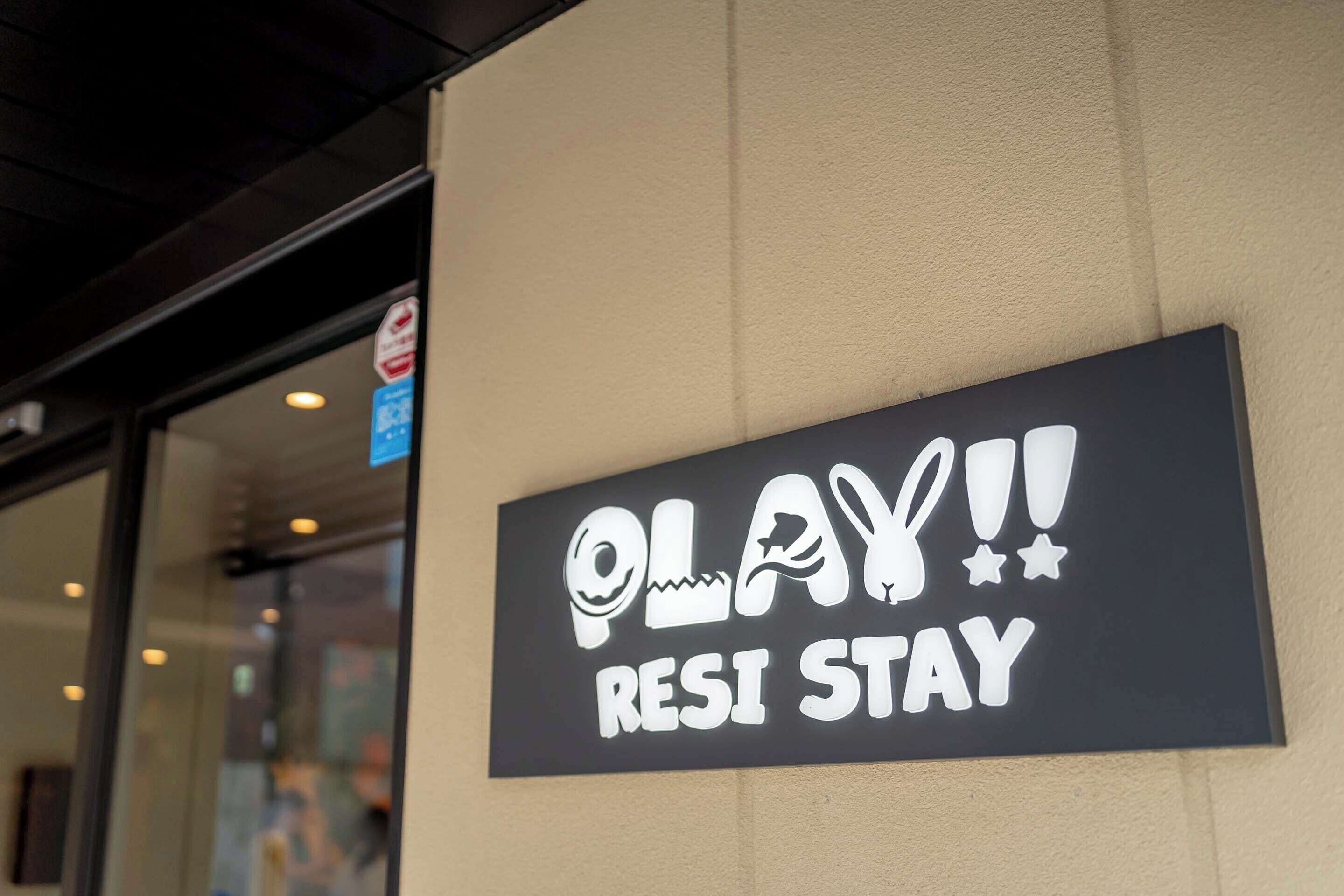 A sign with the text "PLAY!! RESI STAY" on a wall.