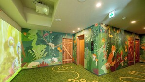 A children's play area with a green carpet, wall murals of animals, and a wooden door.