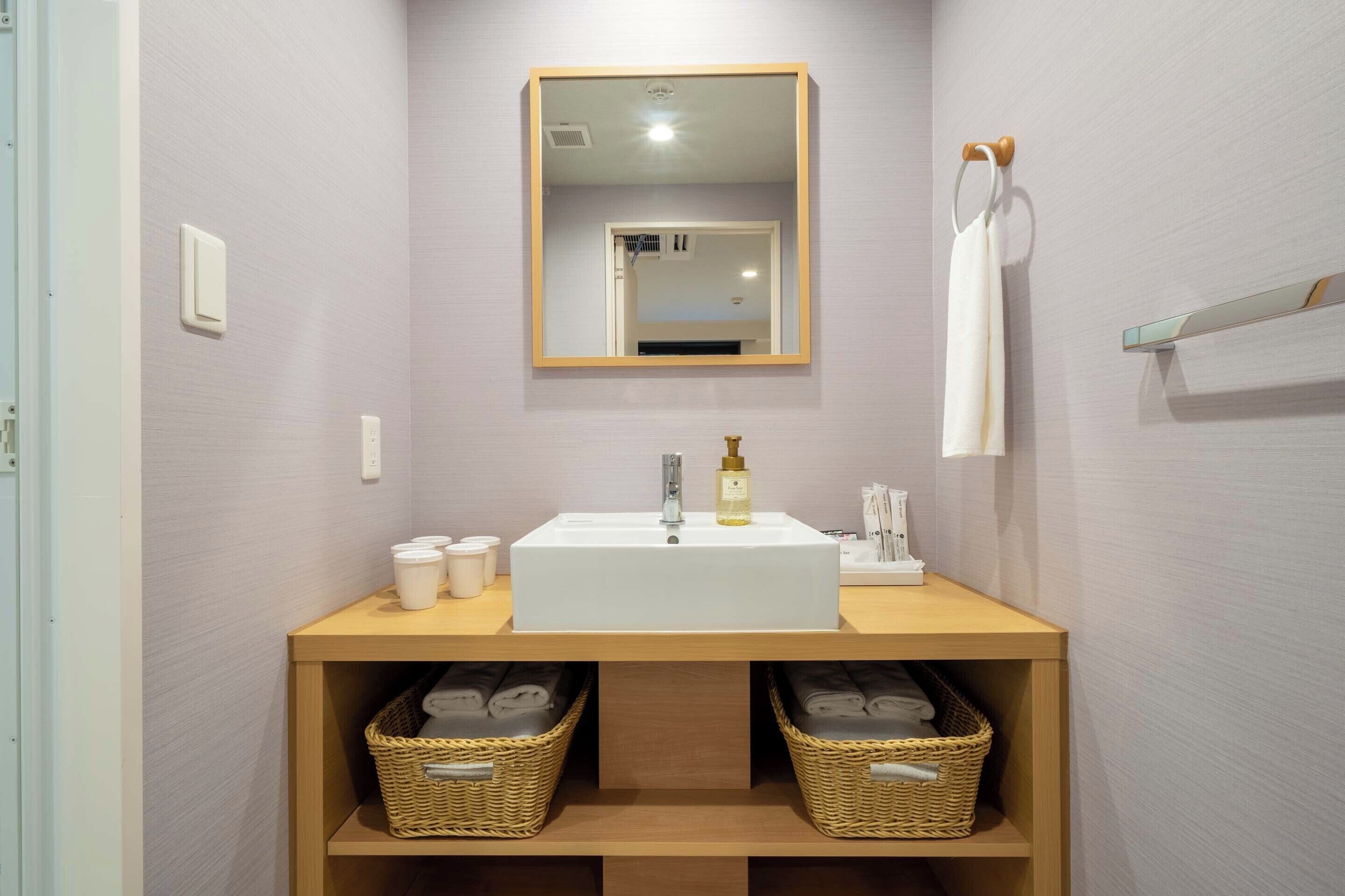 A bathroom with a white sink, mirror, and two wicker baskets under the counter.