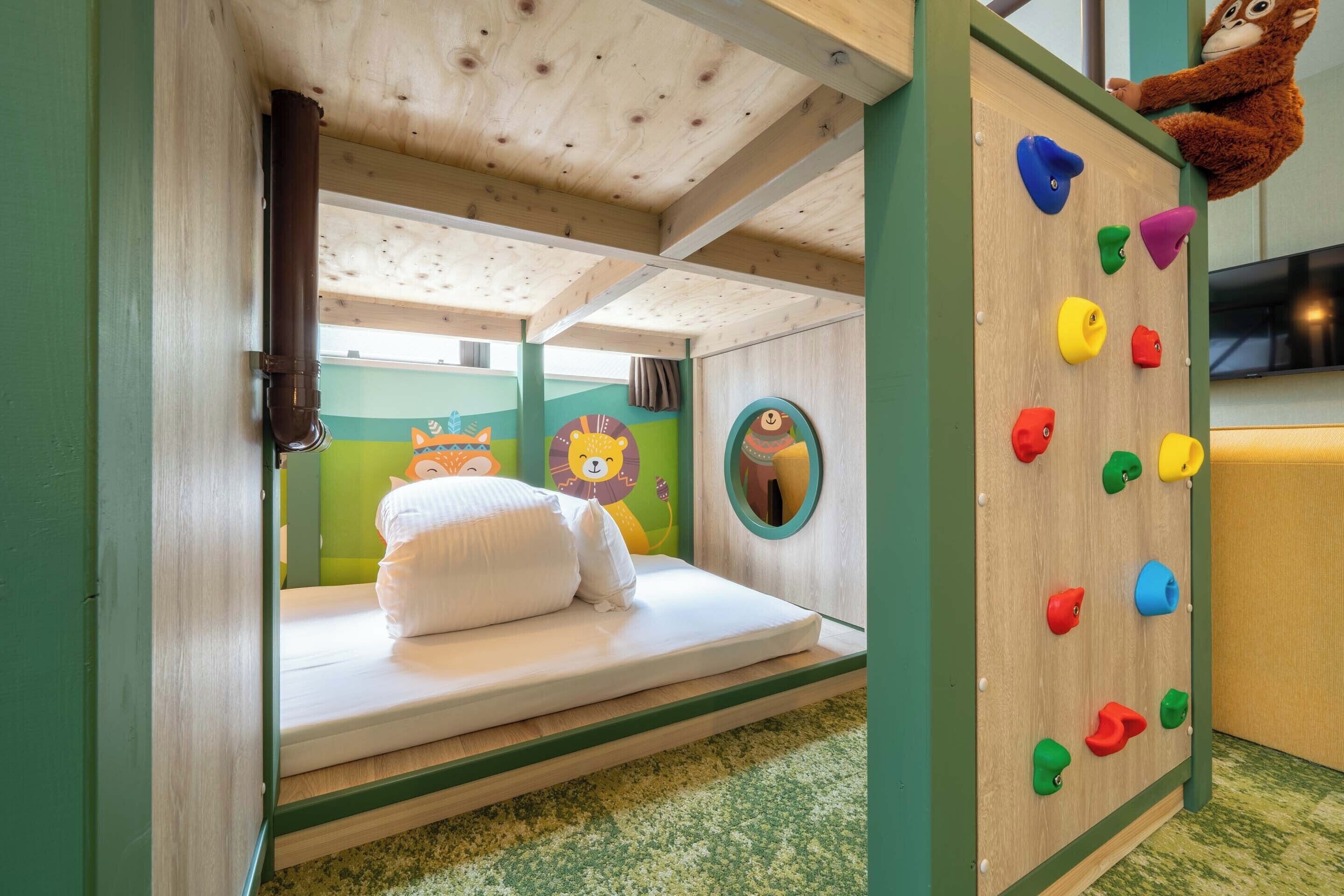 Une chambre d’enfant avec un lit superposé, un mur d’escalade et un jouet en peluche.