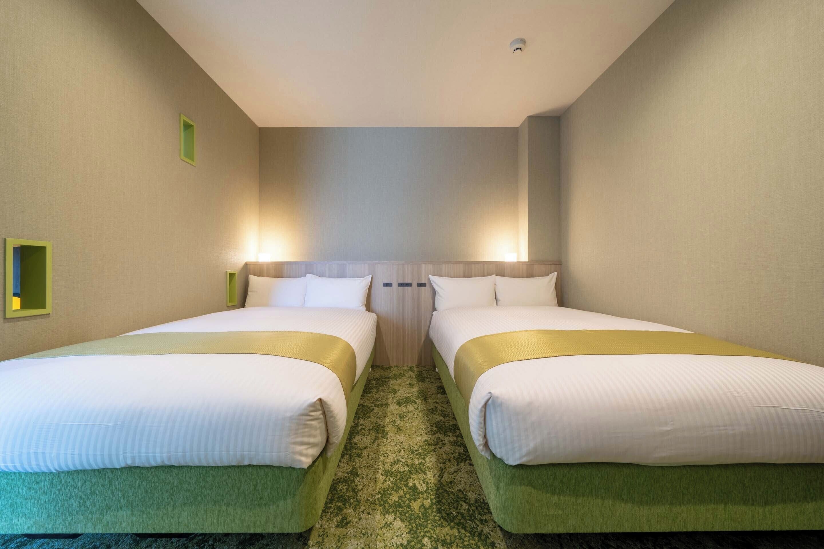 A hotel room with two beds, a carpeted floor, and a ceiling light.