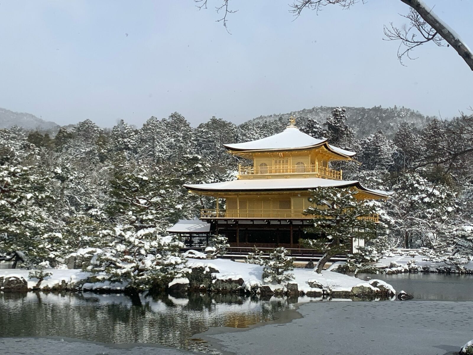 Een traditioneel Japans gebouw met een symmetrisch dak en een centrale ingang, omringd door met sneeuw bedekte bomen en een waterpartij.